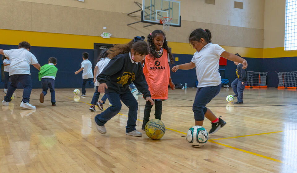 Students playing soccer within the gymnasium.